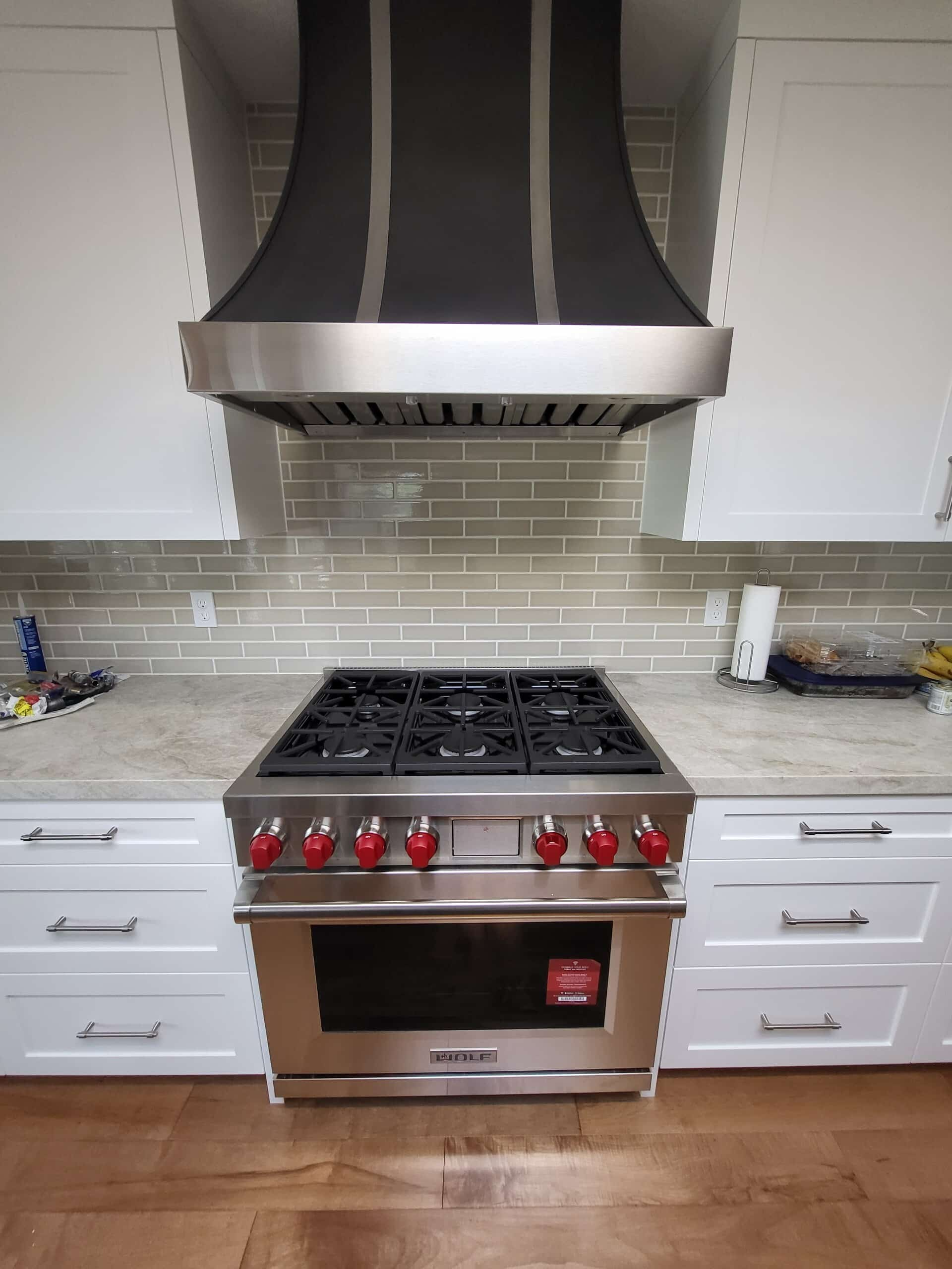 Professional gas range and custom hood installed in a white kitchen